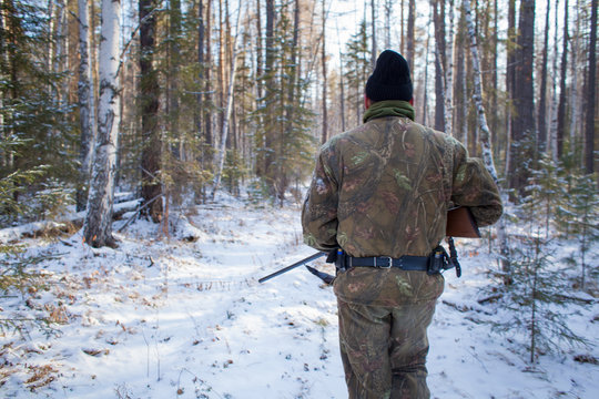 a hunter in the winter woods with a gun in camouflage clothing.