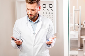 Eye doctor choosing between eyeglasses and lenses standing in front of the eye chart in the cabinet