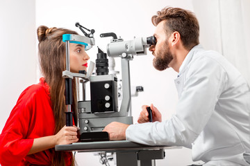 Eye doctor checking vision of young female patient with ophthalmologic device in the cabinet