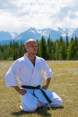 Man in kimono meditating on mountains background.