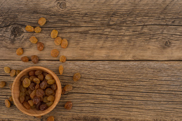 Raisins in a wooden bowl on the old wooden table.