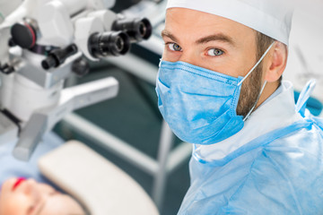 Portarit of eye surgeon at the working plase near the microscope in the operating room