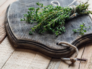 A bunch of fresh thyme herbs on dark bread board on wood background
