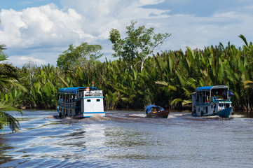 A small boat and two boats floating on the river through dense jungle in clear weather (Singapore)