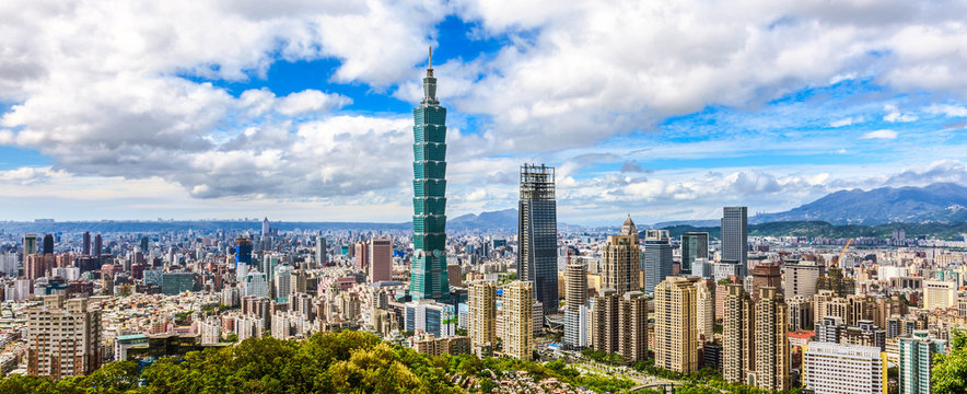 Aerial panorama over Downtown Taipei, capital city of Taiwan with view of prominent Taipei 101 Tower amid skyscrapers in Xinyi Financial District & overcrowded buildings in city center under sunny sky