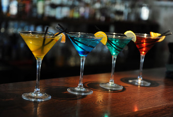 Four colored cocktails on the bar. Yellow, blue, green, red. Decorated with a lemon slice