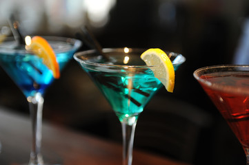 Three cocktails on the bar. Blue, green, red. Decorated with a lemon slice