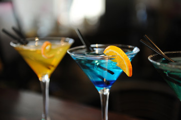 Three cocktails on the bar. Yellow, blue, green. Decorated with a lemon slice