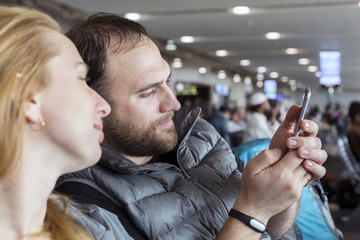 Man and woman at airport terminal using mobile phone