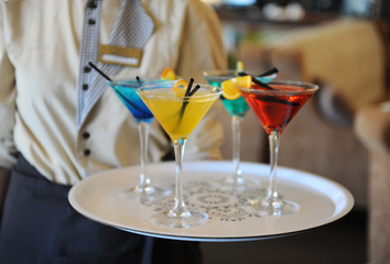 Four colored cocktails on a tray in the hands of the waiter. Yellow, blue, green, red. Decorated with a lemon slice