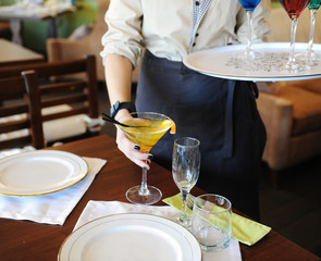 The waiter takes on the table yellow cocktail. White plates on the table
