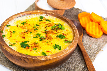 Pumpkin cream soup with saffron and parsley in a wooden bowl