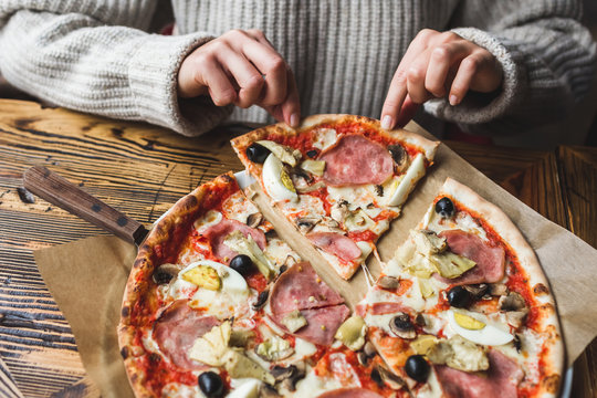 Woman hands take a piece of fresh hot pizza with ham, artichokes