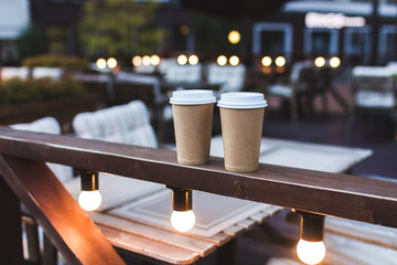 Two cups takeaway coffee on cafe veranda with bokeh lights
