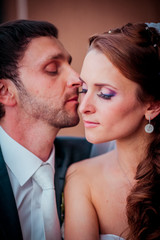 Lovely moment of the newlyweds in the cafe. Bride and groom sitting near large window and kissing each other.