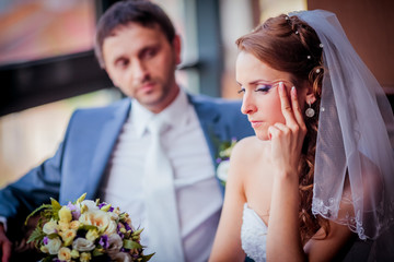 Lovely moment of the newlyweds in the cafe. Bride and groom sitting near large window and kissing each other.