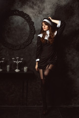 attractive sexy nun in stockings and shoes stands near a wall in a dark room