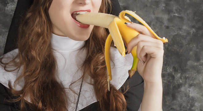 nun holding a banana and bites him on a dark background