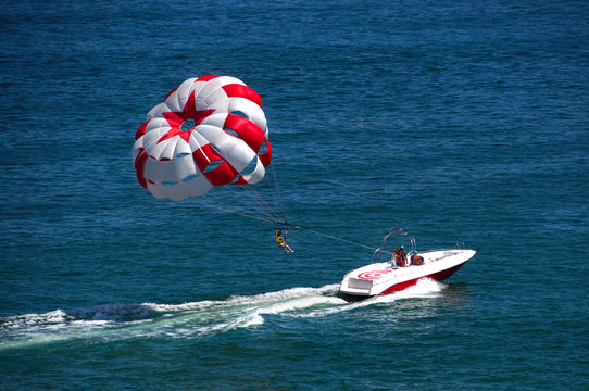 Parashuting water amusement. Flying on a parachute behind a boat on a summer holiday by the sea in the resort. Beautiful bright blue water and red and white parachute.