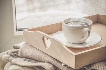Obraz na płótnie Canvas Tea on tray and sweater in from of snowing winter