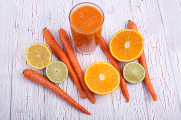 orange detox coctail with oranges,lime and carrots lies on white