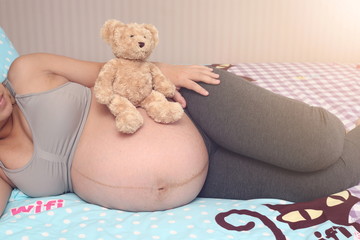 Teddy Bear sitting on pregnant Asian woman sleep on the bed,Close up shot.