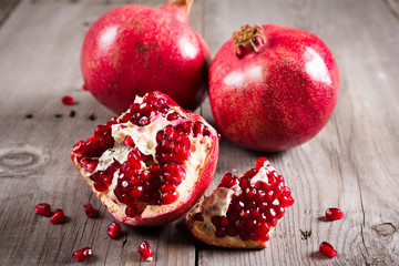 Whole and broken red ripe juicy pomegranates on rustic wooden unpainted table