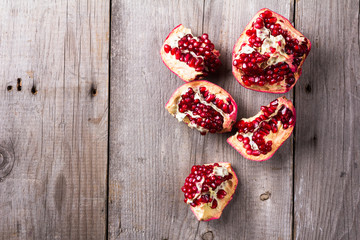 Broken red ripe juicy pomegranates on rustic wooden unpainted table