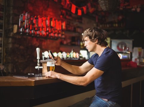 Man with glass of beer using mobile phone in counter