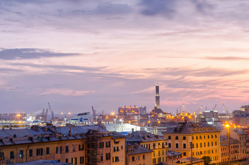 Naklejka premium View over the rooftops of Genoa at sunset to the city's oldest structure and famous landmark the lighthouse, with the harbor and the streets lit up with evening city lights