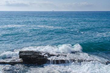 Fototapeta premium Waves hitting a rock near the shore of Nervi, Genoa, in Italy with a boat visible in the distance on the horizon.