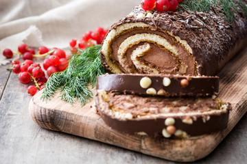 Chocolate yule log christmas cake with red currant on wooden background.closeup

