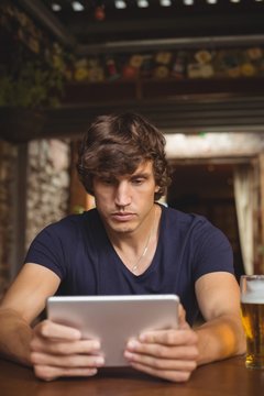 Man using digital tablet with beer glass on table