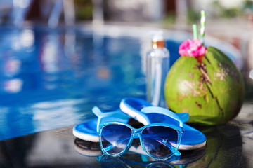 Coconut drink juice with oil, slippers and sunglasses on border of a swimming pool - holiday tropical concept