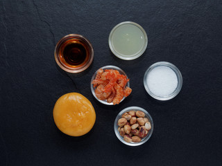 Mix ingredients of Thai green papaya salad (Som tum) composed of dried shrimp, peanut, plum sugar, lime juice, seasoning powder, and fish sauce on dark background