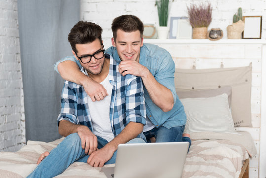 Gay couple sitting on the bed and using a laptop.