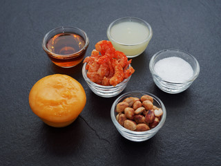 Mix ingredients of Thai green papaya salad (Som tum) composed of dried shrimp, peanut, plum sugar, lime juice, seasoning powder, and fish sauce on dark background