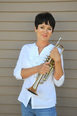 Female trumpet player holding her horn outside.