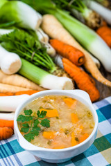 Vegetable soup in a bowl and fresh vegetables on wooden table