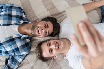 Delighted gay couple making selfie in bed