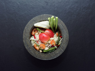 Thai green papaya salad (Som tum) in granite mortar on dark background