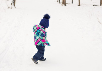 Fototapeta na wymiar Happy toddler girl playing in a beautiful snowy winter park on Christmas day