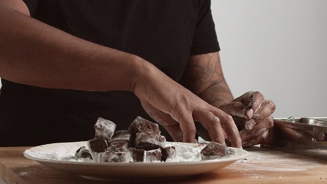 Slow motion, chief takes bunch of chocolate pieces and drops them to a plate with sugar powder inside