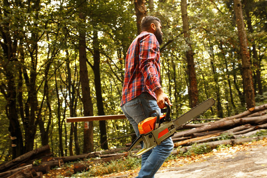 Lumberjack worker walking in the forest with axe and chainsaw.