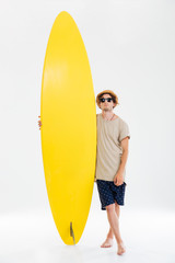 Portrait of a man in sunglasses and hat holding surfboard