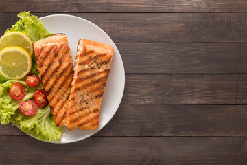Grilled salmon with lemon, tomato on the wooden background. 