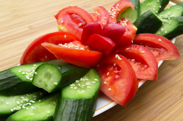 Tomatoes and cucumbers sliced and sprinkled with sesame seeds on wooden background