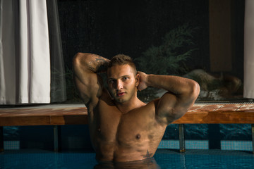 young healthy man with muscular body swims in swimming pool and representing healthy and recreation concept