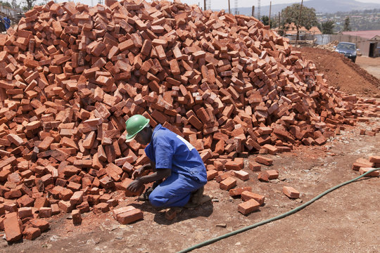 A worker on a building site in Kigali, Rwanda, kneeling next to a pile of red bricks.