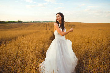 beautiful and young bride in white dress walking in a field